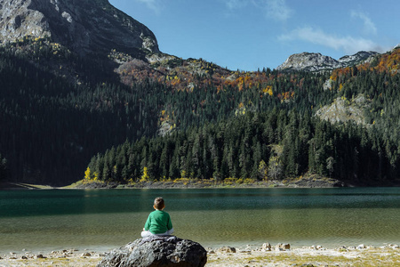 男孩坐在一块大石头上，享受秋天黑湖的意见