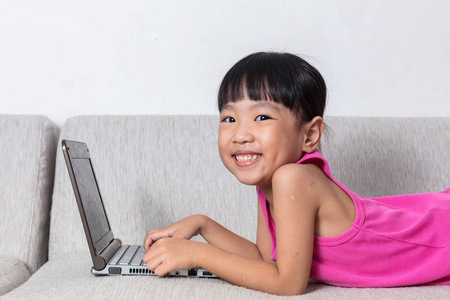 微笑亚洲中国的小女孩躺在沙发上使用笔记本电脑
