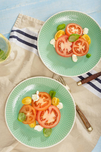意大利沙拉配有西红柿和芝士奶酪, 蓝木桌上有白葡萄酒, 质朴的风格。顶部视图