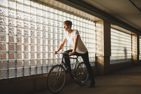 酷男孩骑经典自行车的肖像, 而朦胧的看一边。年轻体贴的人在白色 tshirt 站立与自行车与玻璃墙壁在背景