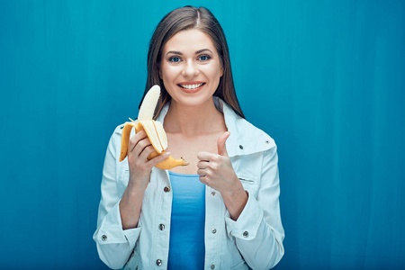 微笑的妇女拿着香蕉和显示拇指在蓝色背景
