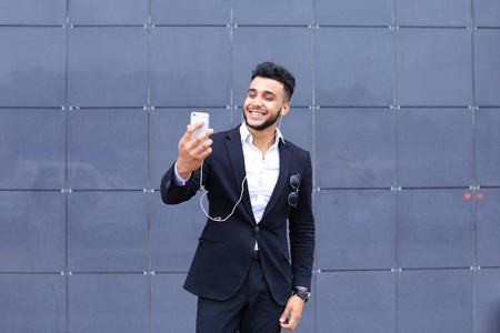英俊的阿拉伯男人需要拍照智能手机在商务中心