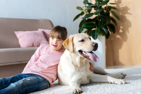 儿童与唐综合征拥抱拉布拉多猎犬在地板上