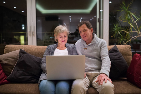 高级夫妇与笔记本电脑坐在客厅里的沙发上