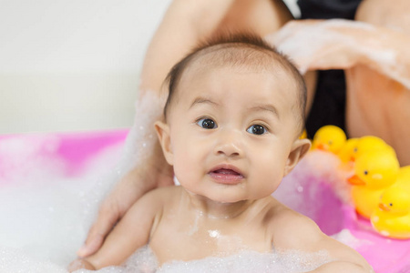 婴儿洗澡在浴缸和玩泡沫气泡