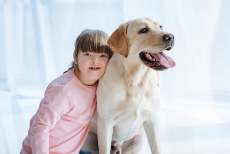 小女孩与唐综合征拥抱拉布拉多猎犬在光背景下