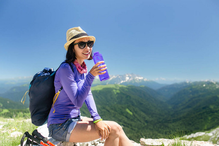 女性旅行者在山上坐拥山和从一个瓶子里喝水