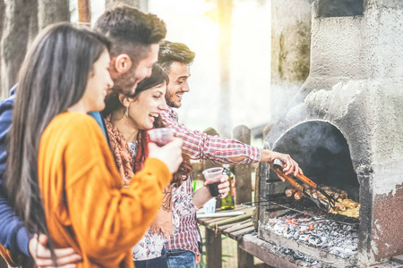 年轻人在后院举行烧烤派对在山上快乐的朋友烧烤肉类和饮用红酒户外友情, 生活方式和食物概念关注男性手权