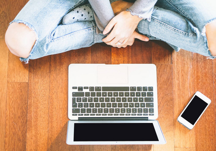 使用膝上型电脑的年轻妇女在她的公寓的木地板上-女孩看她的笔记本