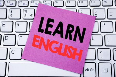 手写公告文本显示学习英语。语言学校的商业概念在白色键盘背景上写在粘纸条纸上
