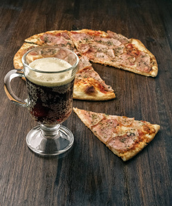黑暗的啤酒杯和比萨饼上木背景