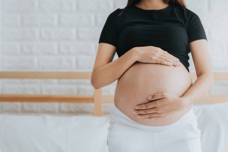 孕妇在床上的窗户附近抱着怀孕的怀孕妇女的图像