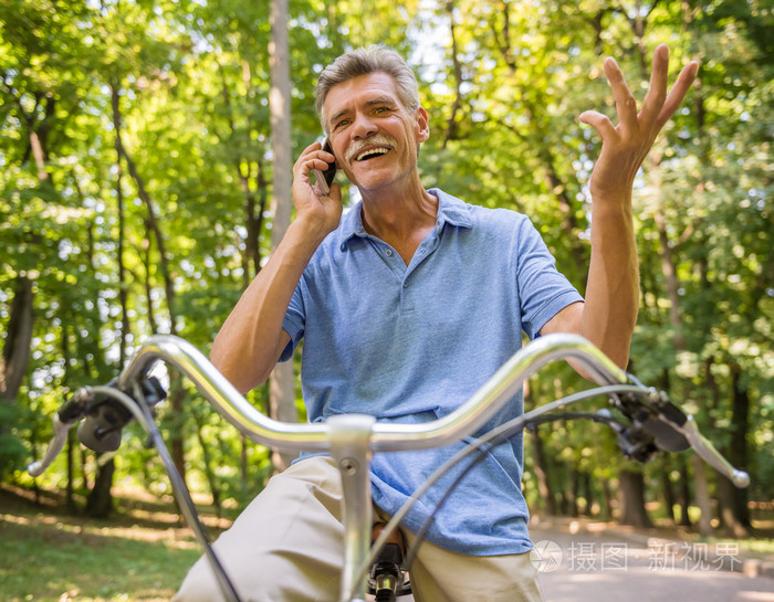 有自行车的老人在公园里用电话说话。