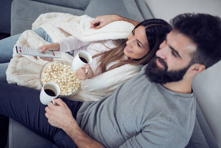 年轻夫妇在他们的公寓放松, 躺在沙发上, 看电影和吃爆米花