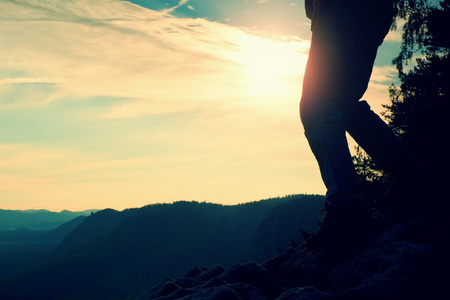 穿着旅游靴的女徒步旅行者腿站在山岩峰上。