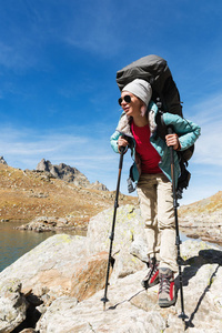 在与一个背包和跟踪棍棒太阳镜的徒步旅行者女孩上升到岩石高的背景下的岩石和高山湖泊