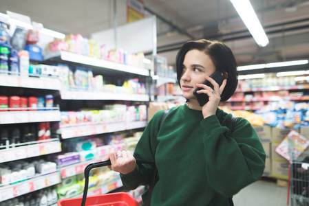 漂亮的小女孩在超市里打电话, 一边看着。那个女孩在超级市场购物
