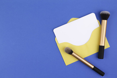 用刷子和黄色信封在蓝色背景上的空白卡