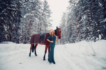 照片的一个美丽的女孩，在绿色的衣服，戴帽从狐狸和马在性质上冬季全长