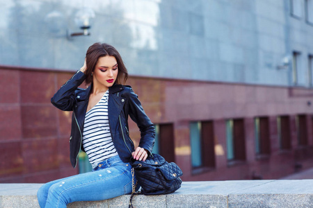 穿着时髦衣服的年轻黑发女孩微笑着坐在户外与背包