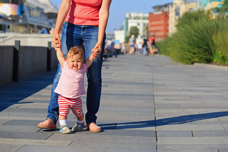 母亲和婴儿学走路在城市公园照片
