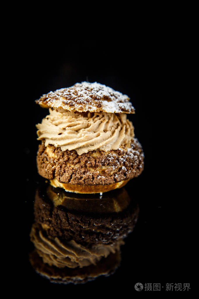 profiterole美味法式甜点的垂直视图与焦糖奶油馅在黑色镜子背景下与