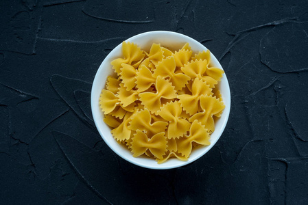 farfalle 通心粉糊在一个白色的杯子上的黑色纹理背景, 在中心特写从顶部