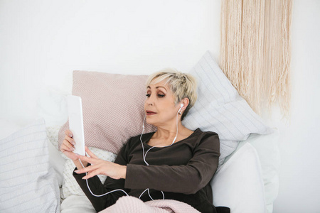 一位年长的积极的女性使用平板电脑观看视频, 听音乐, 和朋友在社交网络上聊天。
