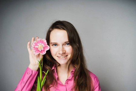 穿粉红色衬衣的女人微笑着捧着一朵花