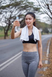 年轻运动妇女与瓶水在公园里