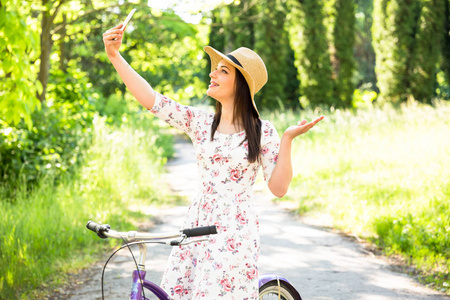 快乐漂亮的年轻女孩骑自行车和自拍在夏季公园。在城市愉快的放松时间。美丽的女人, 晴朗的日子