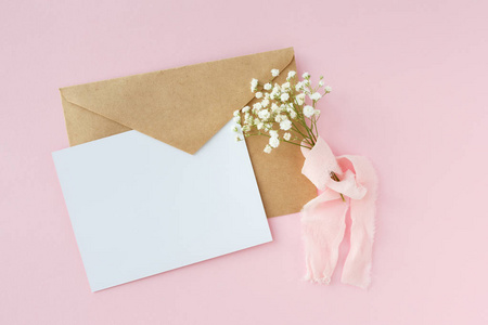 粉红色背景上的一封信, 上面有丝绸丝带,婚礼请柬,一张满天星和一个