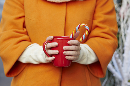 女人手里拿着带杯子和圣诞糖果的羊毛手套