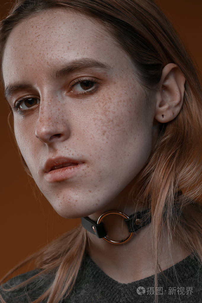 一个漂亮的女孩与演播室棕色背景上的雀斑的肖像