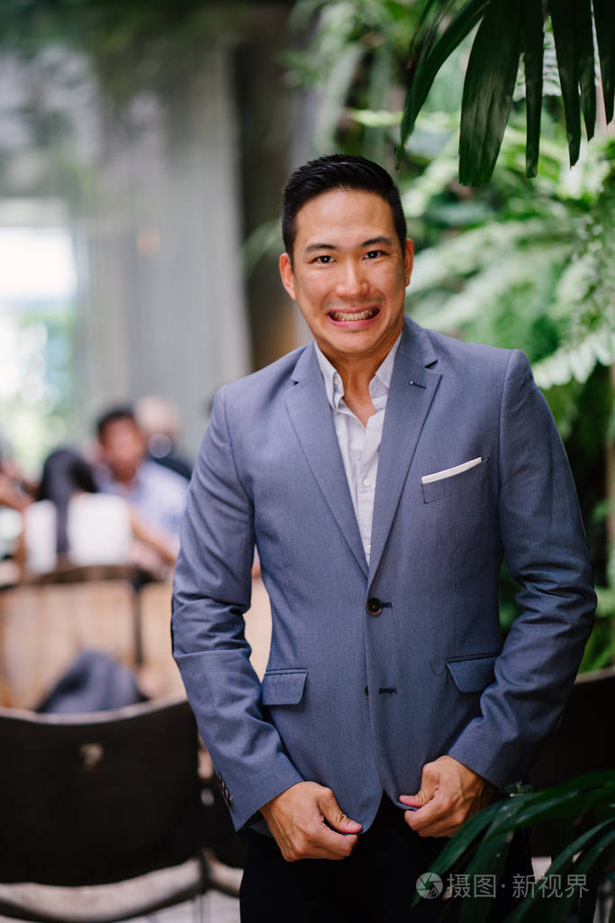 一个英俊, 年轻, 聪明的中国亚裔男子的肖像微笑着, 站在绿色的墙上的