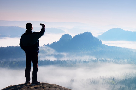 高旅游正在自拍照在山谷上空的山峰上。智能手机摄影