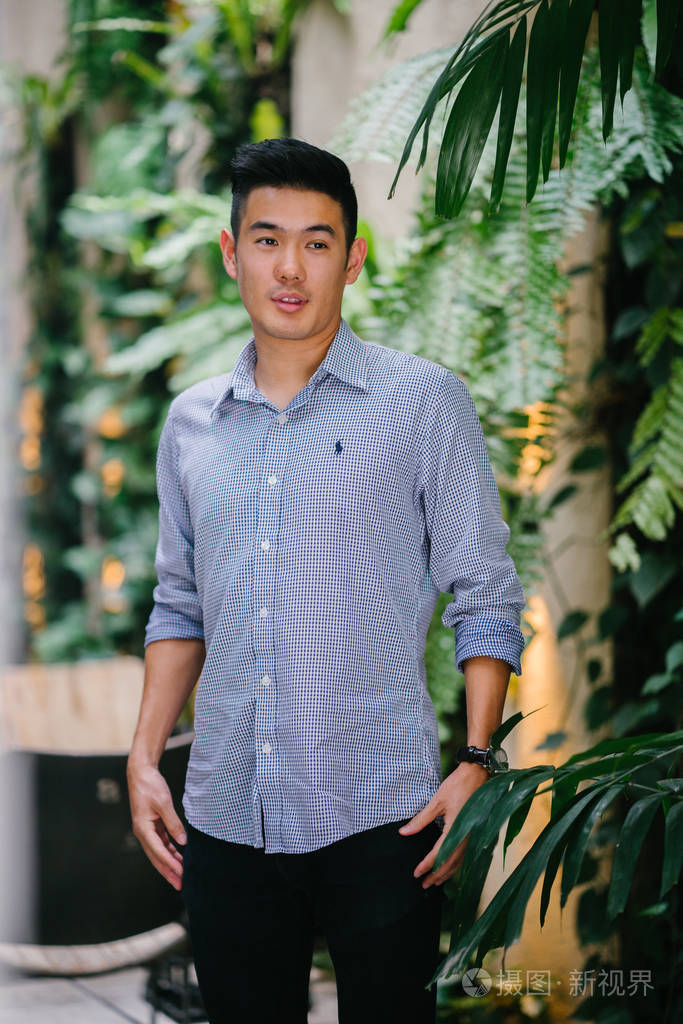 一个英俊, 年轻, 聪明的中国亚裔男子的肖像微笑着, 站在绿色的墙上的