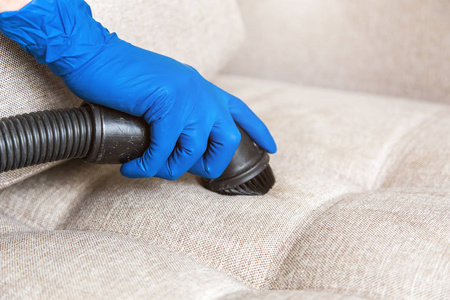 男看门人在手套和制服真空清洁沙发与专业设备照片