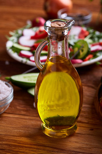 金黄橄榄油在板材前面透明玻璃罐子与蔬菜沙拉, 浅的领域深度