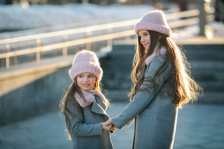 两个可爱的小妹妹牵着手在城市街道上穿着灰色大衣和粉红色的帽子照片