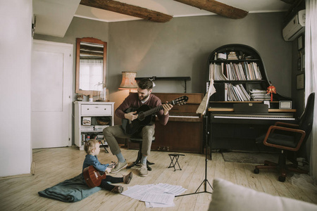 年轻的父亲和小女儿在家里玩声学吉他在房间里