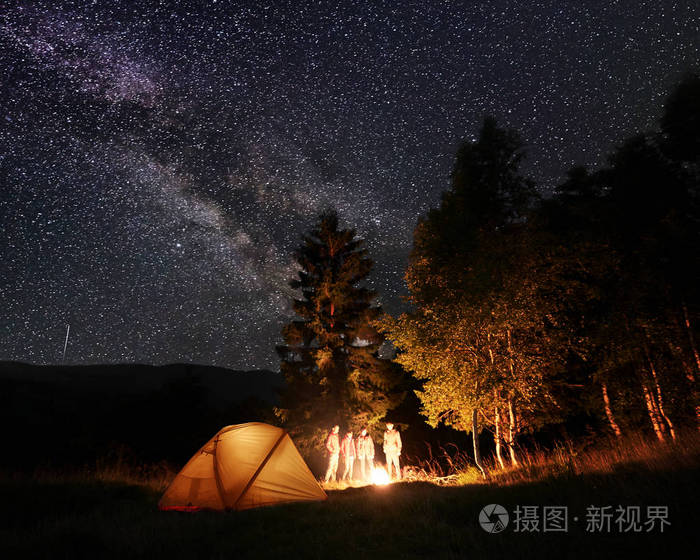 一群游客在夜间露营, 在灯火通明的帐篷森林附近, 看着在山和山的背景