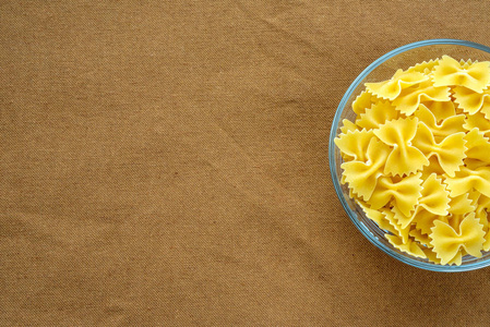 farfalle 通心粉面食在一个玻璃杯上棕色郊区背景纹理与一侧。顶部特写。文本空间