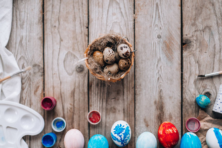 彩色鸡蛋的最高视图, 巢与鹌鹑蛋, 刷子, 礼品盒和油漆的木板背景