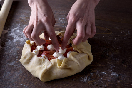 前视图的过程中烹调蔬菜饼干, 比萨饼。妇女的手放在西红柿和南瓜上的面包在轧面团上的干酪奶酪