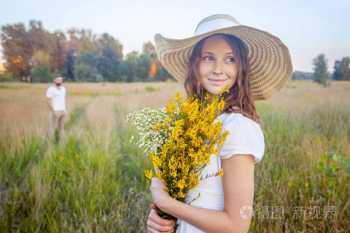 美丽的女人抱着黄色花束和盯着相机和她的男朋友的背景