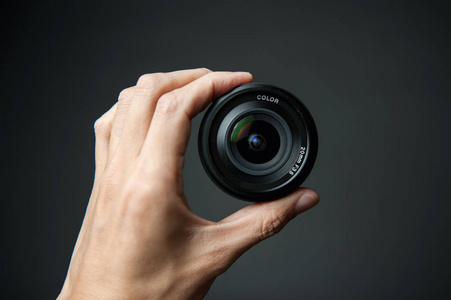 在黑色背景下手持相机镜头的人的手照片