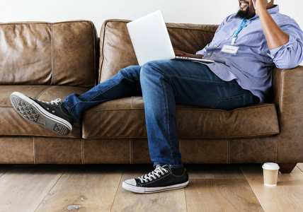 黑衣人在沙发上放松, 手持笔记本电脑, 地板上的咖啡杯