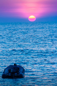 美丽的日落在海与橙色, 圆和明亮的太阳在黄昏在平静的海洋在剧烈的天空背景。剪影船和不明船司机在前景。从卡马拉海滩查看