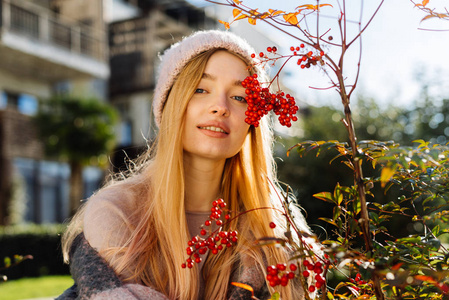 美丽的年轻女子坐在红色浆果的灌木丛旁边在一个晴朗的日子
